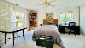Une chambre à coucher comprenant un lit, un bureau, une chaise, une bibliothèque et un ventilateur de plafond.