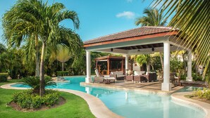 A pool area with a covered seating area, palm trees, and a clear blue sky. - Two Luxury Villas in Cocotal for Large Groups – With Jacuzzi, Pools, Gym (Punta Cana)