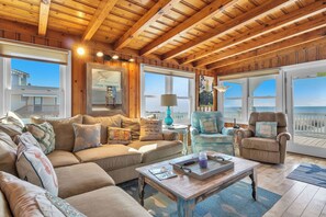 A cozy living room with a wooden ceiling, large windows, a sofa, a chair, and a coffee table.