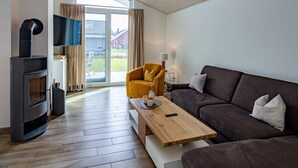 A modern living room with a sofa, a wooden coffee table, a TV, and a fireplace. - Ferienhaus mit Sauna im Ferienpark Mirow (Mirow)