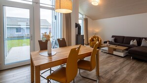 A modern living room with a wooden dining table, yellow chairs, a sofa, and a large window. - Ferienhaus mit Sauna im Ferienpark Mirow (Mirow)