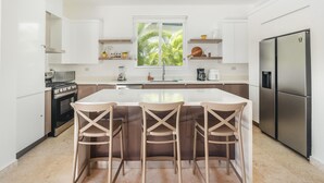 A modern kitchen with white cabinets, a central island with bar stools, a built-in oven, and a refrigerator.