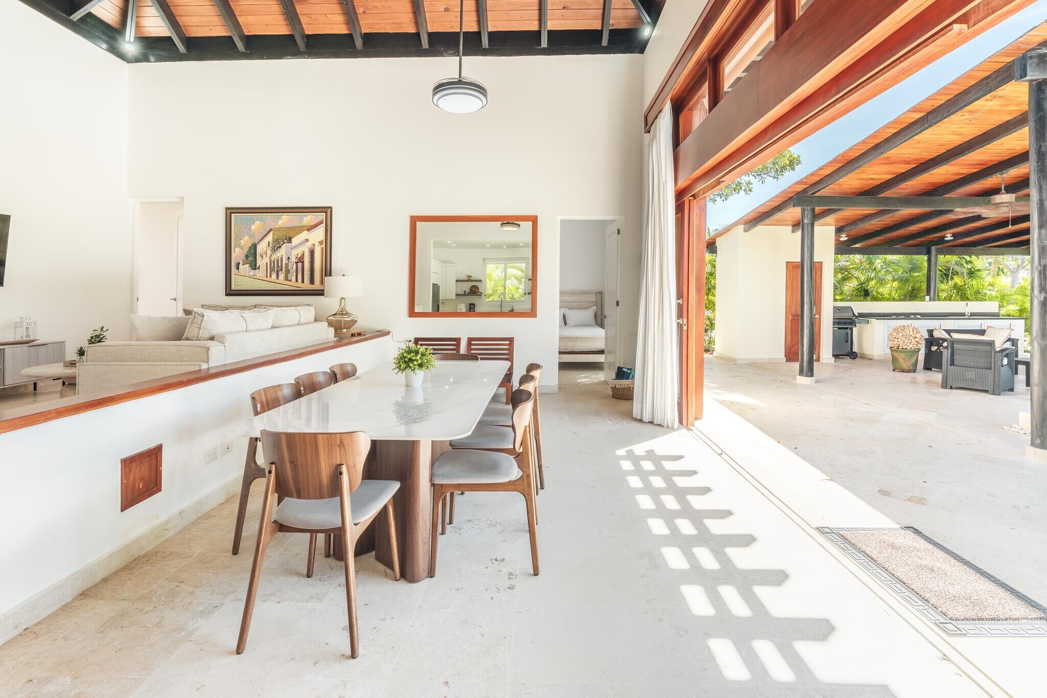 A spacious dining area with a long table and chairs, a large mirror, and a painting on the wall.