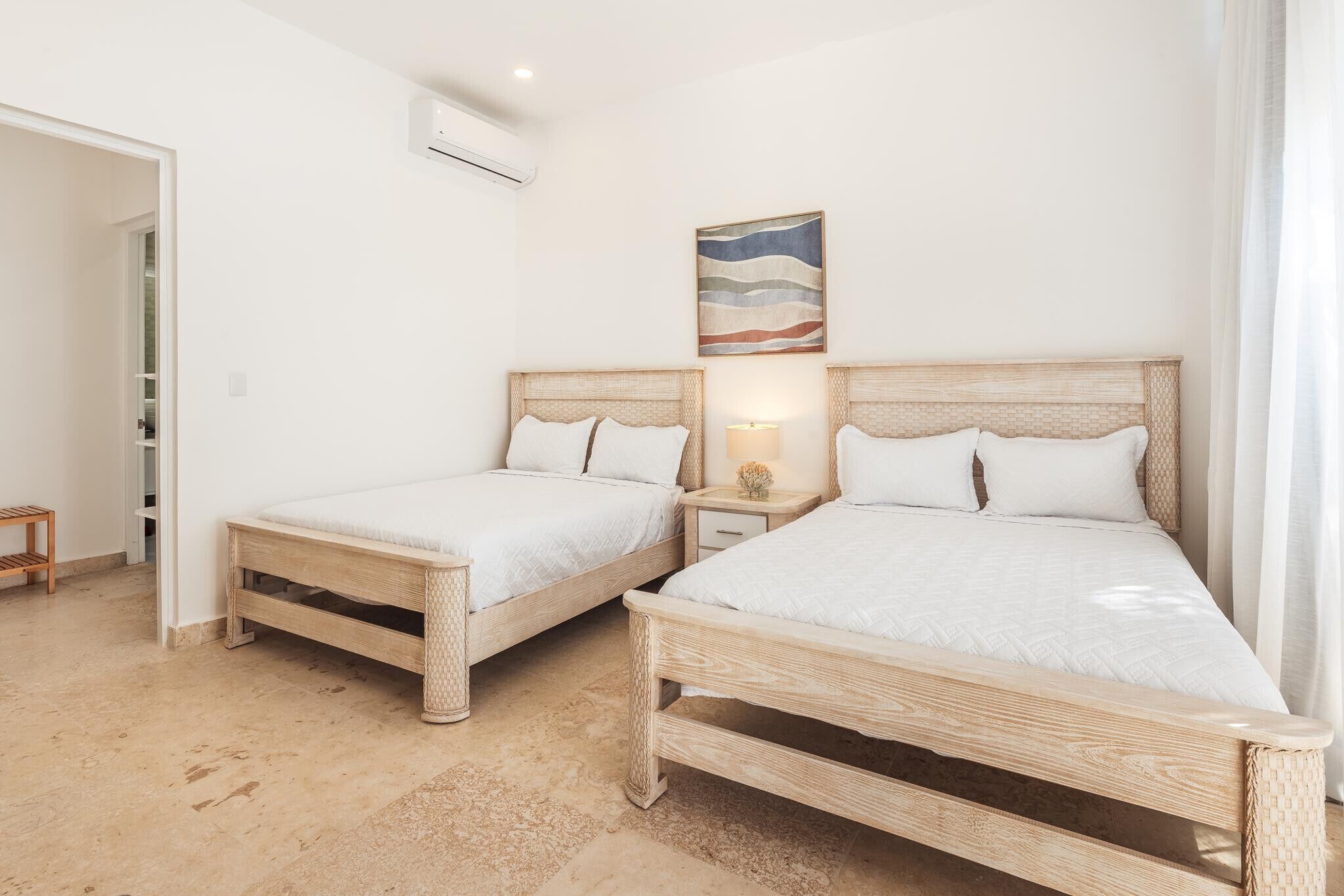 A bedroom with two wooden beds, a nightstand with a lamp, and a wall-mounted air conditioner.