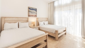 A hotel room with two wooden beds, a nightstand with a lamp, and a large window with sheer curtains.