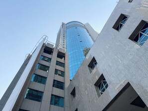 A modern high-rise building with a curved glass facade and a series of windows. - Sunset Downtown Studio l Near Metro & Shops (Dubai)
