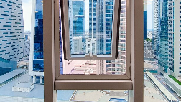 Blick durch ein Fenster eines modernen Gebäudes auf einen klaren Himmel und andere Hochhäuser im Hintergrund.