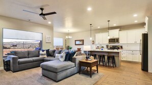 A spacious living room with a gray sectional sofa, a wooden coffee table, and a large window overlooking a tennis court. - Stunning Townhome in Zion Village with private hot tub and lazy river (Hurricane)