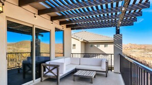 A covered balcony with a white sofa, a wooden coffee table, and a glass door leading to an outdoor area. - Stunning Townhome in Zion Village with private hot tub and lazy river (Hurricane)