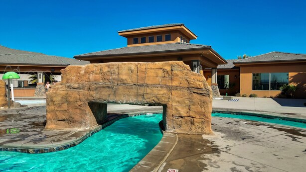 A pool area with a rock arch structure, clear blue water, and a building with a brown roof in the background. - Stunning Townhome in Zion Village with private hot tub and lazy river (Hurricane)