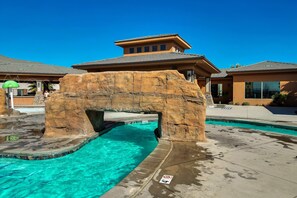 Un espace piscine agrémenté d’une arche en pierre, d’une eau d’un bleu cristallin et, au fond, d’un bâtiment dont le toit est de couleur marron.
