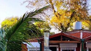 A brick house with a chimney, a patio with chairs, and a large tree. - El Rosedal Cataratas / Apartment - 2 levels (Puerto Iguazú)