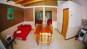 A cozy room with a wooden ceiling, a red sofa, a dining table with chairs, a television, and a small kitchenette. - El Rosedal Cataratas / Apartment - 2 levels (Puerto Iguazú)