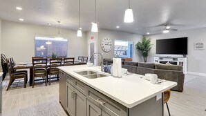 A modern kitchen with a central island, dining area with chairs, a sofa, and a TV in the living area. - Stunning townhome with premiere resort amenities, lazy river and private hot tub (Hurricane)