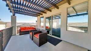A covered outdoor seating area with wicker furniture and red cushions, a glass door leading to a balcony, and a view of the landscape. - Stunning townhome with premiere resort amenities, lazy river and private hot tub (Hurricane)