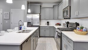 A modern kitchen with grey cabinets, stainless steel appliances, and a white countertop. - Stunning townhome with premiere resort amenities, lazy river and private hot tub (Hurricane)