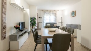 A modern living room with a dining area, a grey sofa, a TV on a built-in shelf, and a potted plant. - Grace s House in Pisa (Pisa)