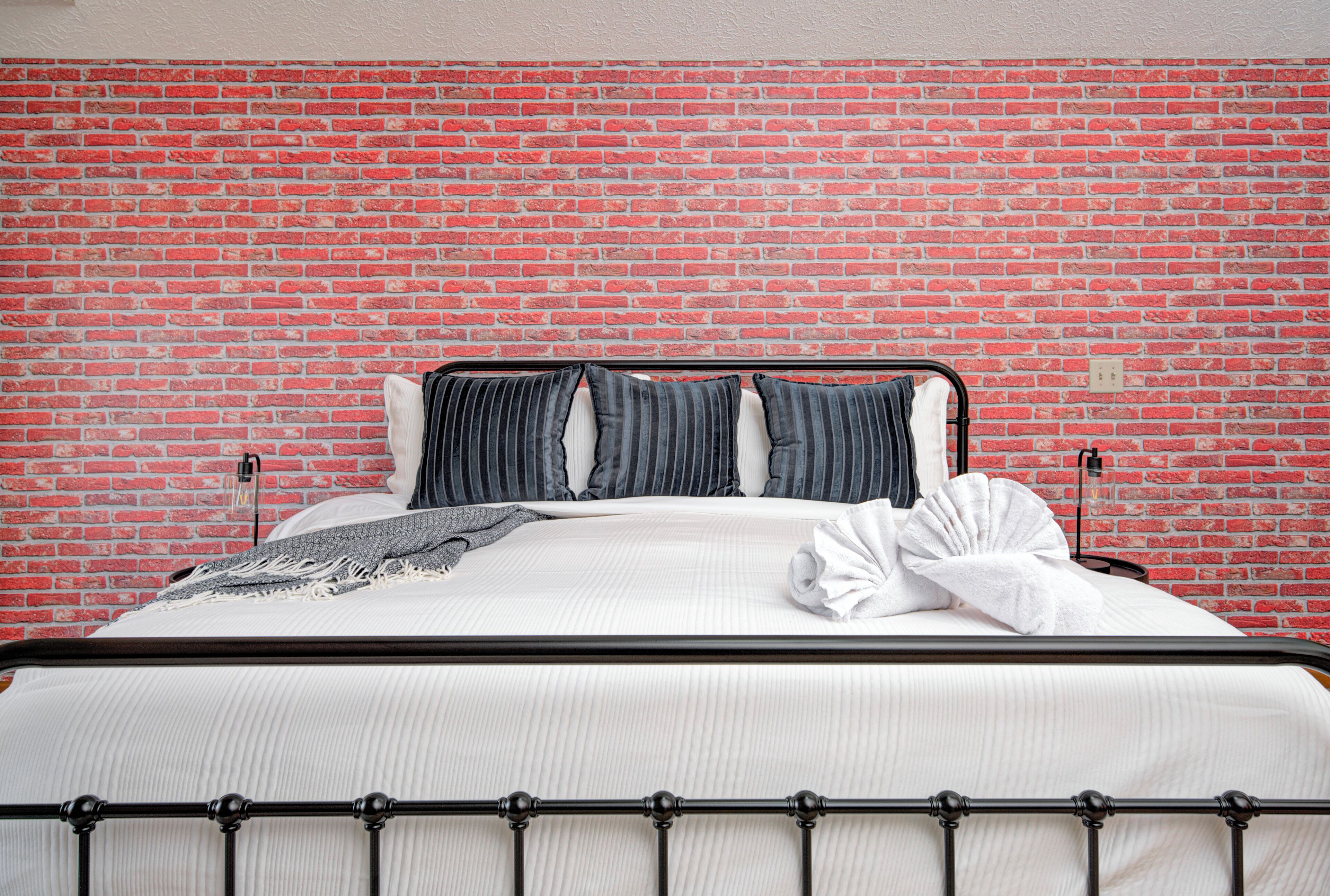A bed with a metal frame, white bedding, and striped pillows against a red brick wall.