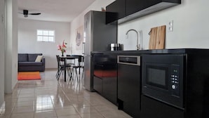 Eine moderne Küche mit einem schwarzen Kühlschrank, Backofen und einer Mikrowelle. Es gibt einen Essbereich mit einem grauen Sofa und einem Tisch mit Stühlen.