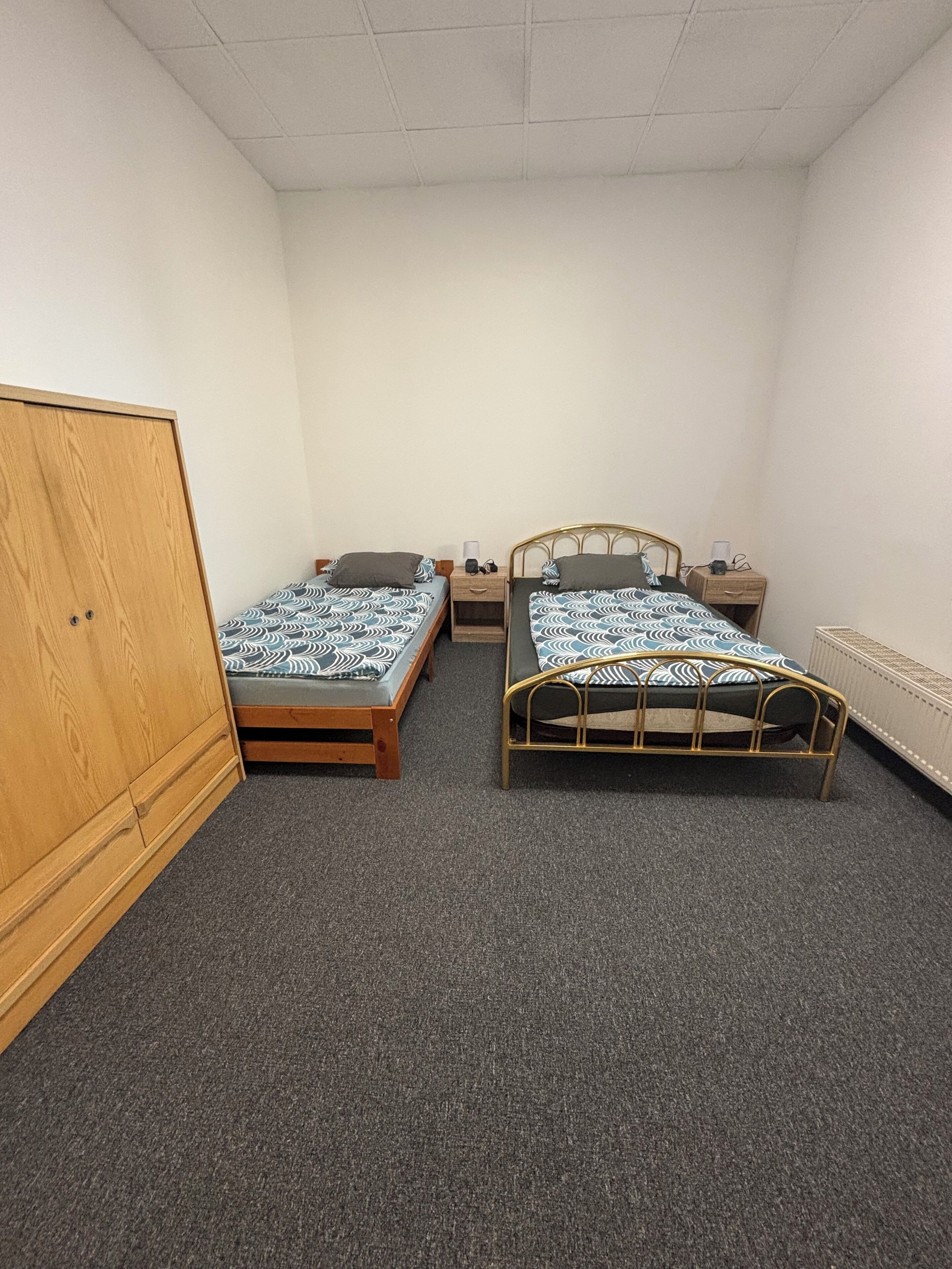 Ein Zimmer mit zwei Einzelbetten, einem Holzschrank und einer Heizung.