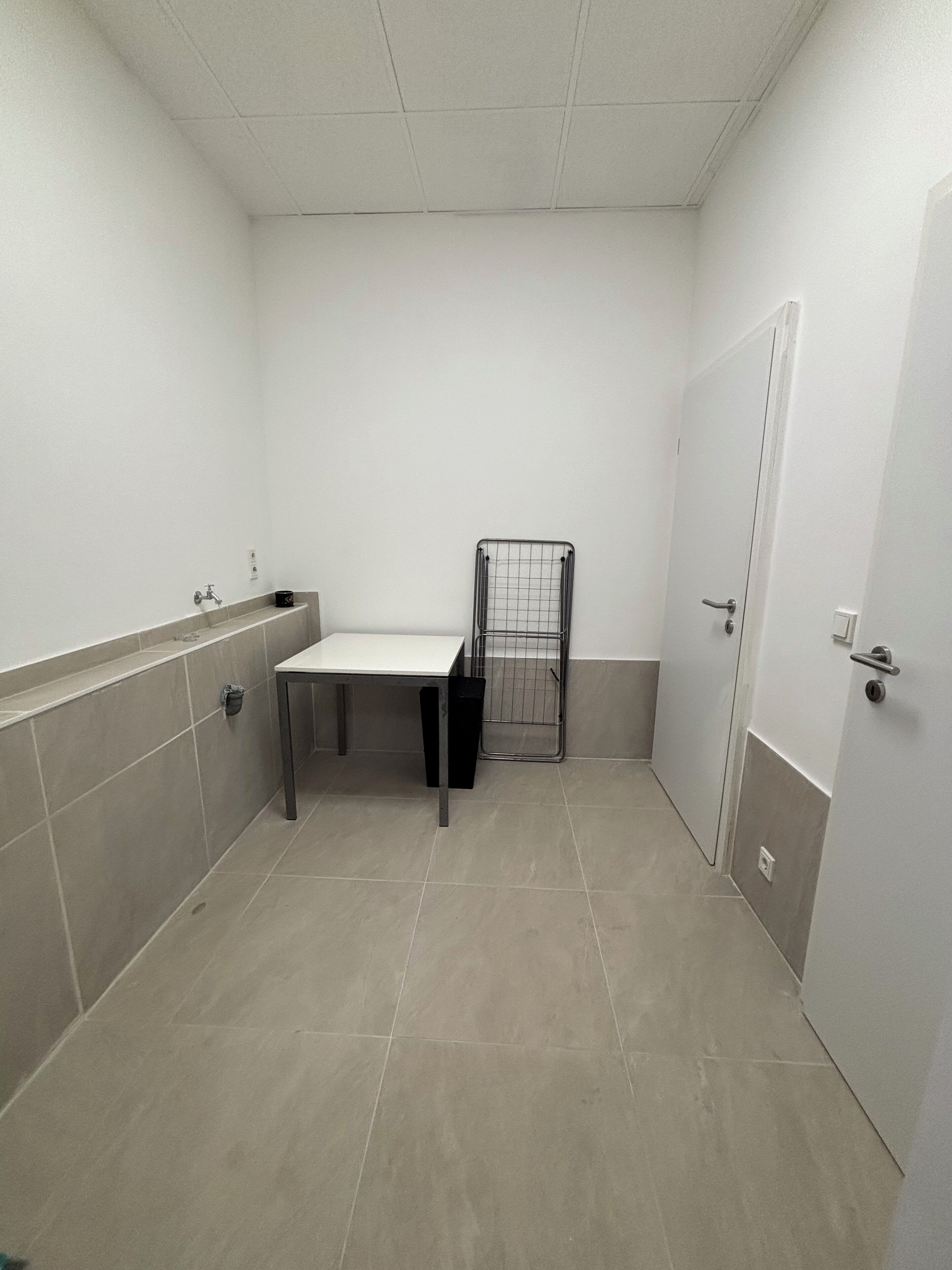 Ein kleines, sauberes Badezimmer mit Toilette, Waschbecken und einem Metallregal.