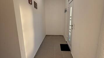 A narrow hallway with a tiled floor, white walls, a ceiling light, and a door with a window.