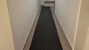 A narrow hallway with white walls, a black carpet, and a small table with a pitcher and a bowl at the end.
