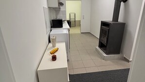 A compact kitchen with a microwave, a kettle, and a small cabinet. There's a black stove with a chimney and a tiled floor.