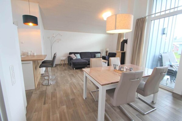 Una sala de estar moderna con un sofá, una mesa de comedor con sillas, una zona de cocina y un ventanal con cortinas.