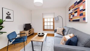 A modern living room with a grey sofa, a blue chair, a wooden coffee table, and a television on a wooden stand. - Bright&Cosy Flat near Scottish Gallery (Edinburgh)