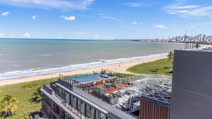 A coastal hotel with a rooftop pool, beach view, and city skyline in the background.