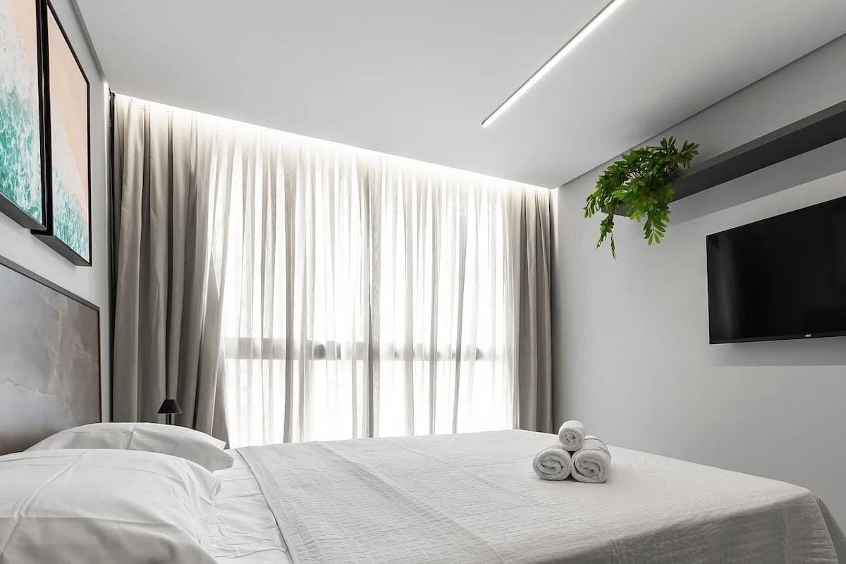 Ein modernes Hotelzimmer mit Bett, Vorhängen, Fernseher und einer Pflanze.