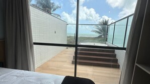 A bedroom with a large window, a bed, and a view of a balcony with steps leading to a pool.