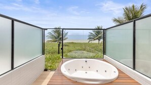 A modern outdoor bathroom with a hot tub, glass walls, and a view of the beach.