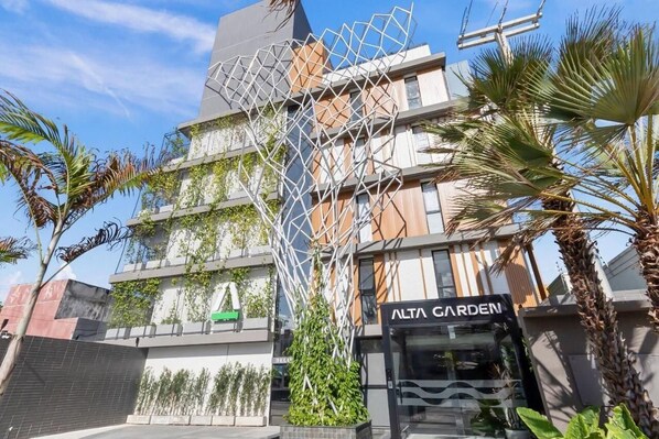 Un edificio moderno con un letrero que dice 'ALTA GARDEN' y una estructura metálica geométrica.
