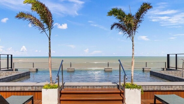 A poolside area with steps leading to the water, lounge chairs, and palm trees.