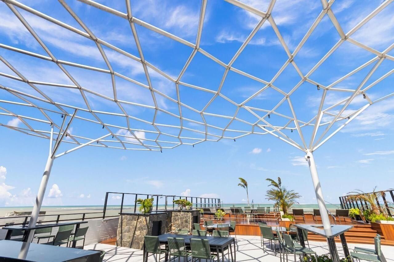 An outdoor seating area with tables and chairs, a clear sky, and a view of the ocean.