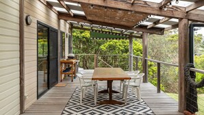 An outdoor patio with a wooden table and chairs, a pergola with string lights, and a view of greenery. - Two Many Birds - Seal Rocks (Seal Rocks)