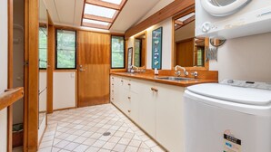 A compact kitchen with a washing machine, a sink, and a window with a view of greenery. - Two Many Birds - Seal Rocks (Seal Rocks)