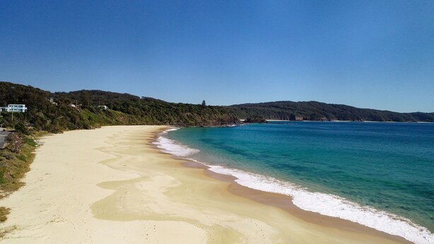 A sandy beach with clear turquoise waters, a few houses on the hillside, and a clear sky. - Two Many Birds - Seal Rocks (Seal Rocks)