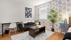 Ein modernes Wohnzimmer mit einem schwarzen Sofa, einem weißen Couchtisch, einem schwarz-weißen abstrakten Gemälde, einem weißen Schreibtisch, einem weißen Sessel und einer Wandtapete mit Städtenamen.