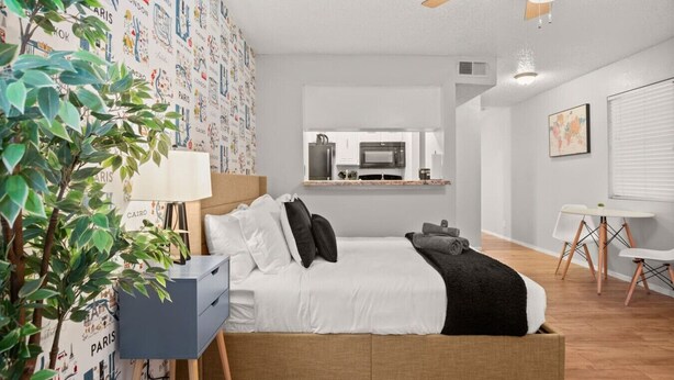 Ein modernes Schlafzimmer mit Bett, Nachttisch, Lampe und Blick auf die Küche.