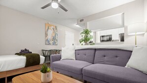 Una habitación moderna y luminosa con sofá, cama, una mesita de madera y un ventilador de techo.