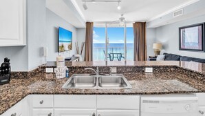 A modern kitchen with granite countertops, a double sink, and a view of the ocean through large windows. - Gulf FRONT! Balcony-Heated Pool-Hot Tubs-By Pier Park-Tidewater 716 (Panama City Beach)