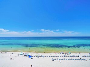 Ein Strand mit klarem türkisblauem Wasser, weißem Sand und mehreren Sonnenschirmen sowie Liegestühlen.