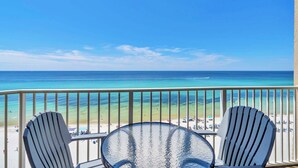 A balcony with two Adirondack chairs and a glass-top table overlooking a beach with clear turquoise water and a sandy shore. - Gulf FRONT! Balcony-Heated Pool-Hot Tubs-By Pier Park-Tidewater 716 (Panama City Beach)
