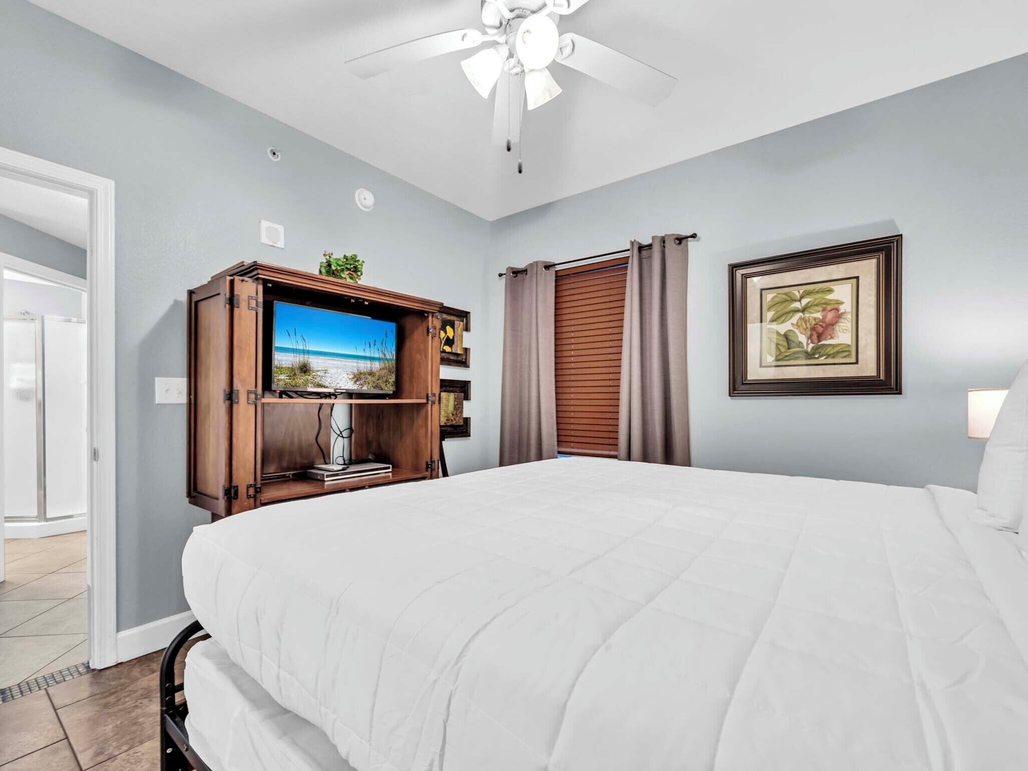 Una camera da letto con un letto grande, una televisione su un mobile in legno, una ventola a soffitto e un quadro appeso al muro.