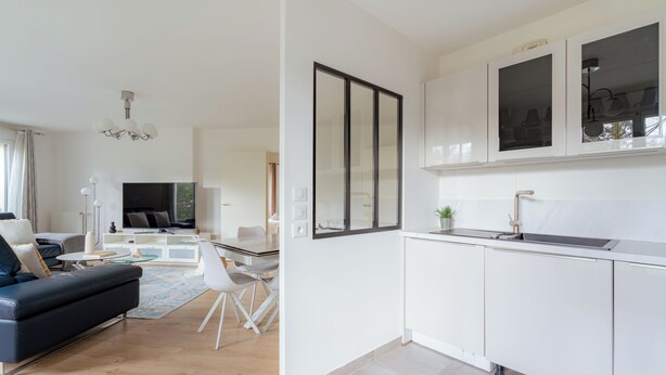 Eine moderne Küche mit weißen Schränken und einem eingebauten Backofen. Ein Essbereich mit einem weißen Tisch und Stühlen ist ebenfalls vorhanden.