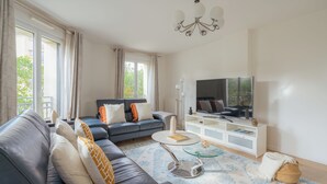 Ein modernes Wohnzimmer mit Sofa, Couchtisch, Fernseher und großen Fenstern.