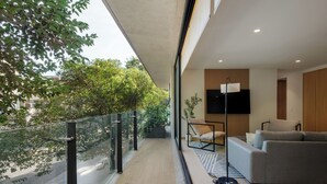 A balcony with a glass railing, a sofa, a floor lamp, and a flat-screen TV.